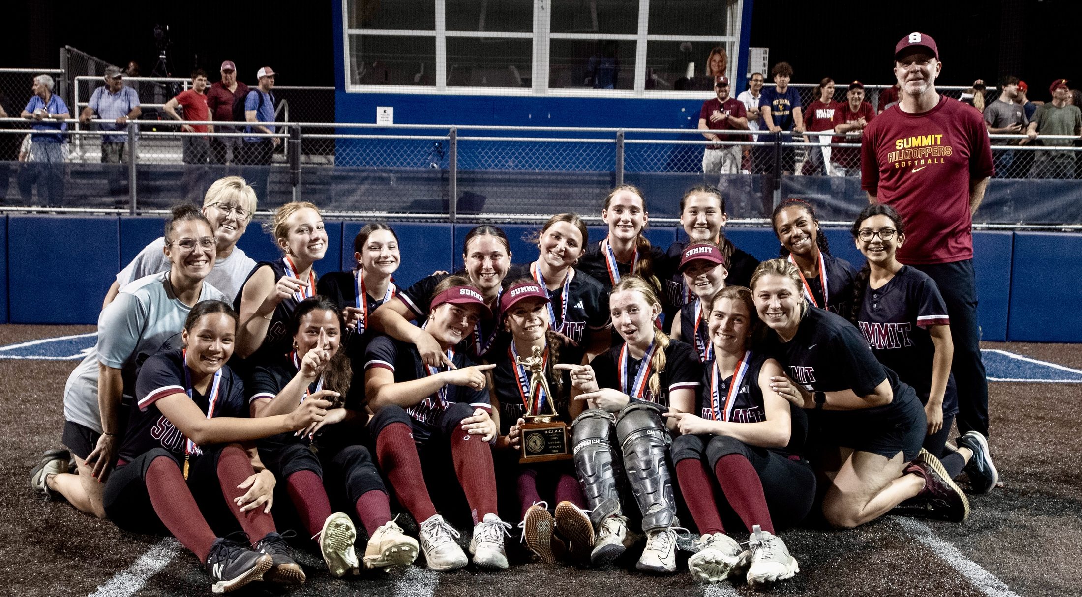 Summit Hilltoppers softball team celebrating on the field with their championship trophy
